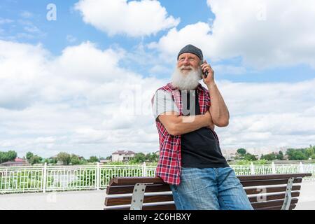Portrait of elderly bearded gentleman in coat talking on cellphone. He is looking away and smiling Stock Photo