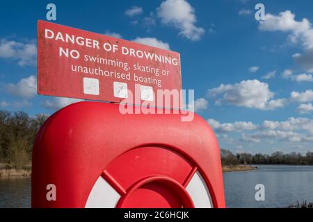 Detailed view of an emergency life ring and warning sign, for use in a water born emergency. The equipment is located next to a large and deep lake Stock Photo