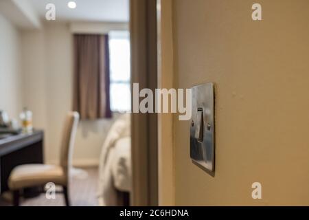 Isolated view of a metal light switch in the office position located in an apartment bedroom. The background shows out of focus table and unmade bed. Stock Photo