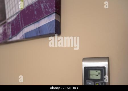 Close-up view of a modern, LCD air-con keyboard and display seen in a modern apartment. Seen near modern, abstract art hanging of the same wall. Stock Photo