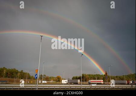Double rainbow over a motoroway with long haul trucks. Colourful autumn landscape with rainbows in a dark stormy sky Stock Photo