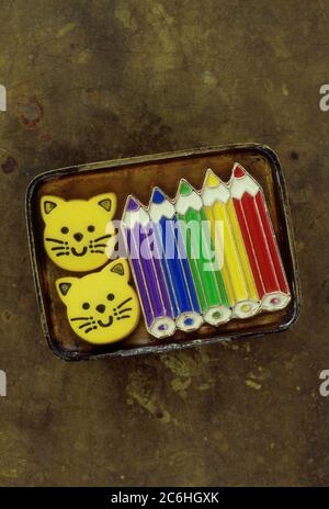 Small brass lid containing enamel brooch or badge or pin of sharpened colour pencils and two plastic smiling cat faces Stock Photo