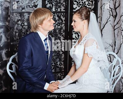 Bride and groom sitting in studio with vintage interior. Photo of happy newlyweds Stock Photo