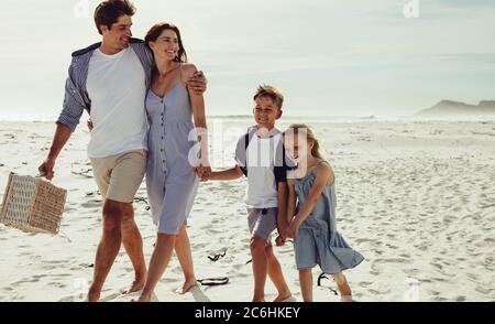 Kids walking with their parent along the beach on summer day. Family of four at beach for a picnic.