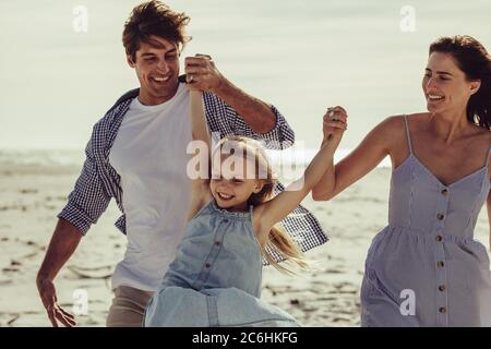 Couple holding hands of their daughter and playing on the beach. Girl having a great time with parents on a vacation.