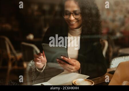 Woman sitting at a coffee shop and using her digital tablet. Female using tablet computer while sitting inside a cafe. Stock Photo