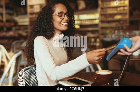 Smiling woman paying contactless using her credit card in a cafe to pay her bill. Female customer making a card payment in a restaurant. Stock Photo