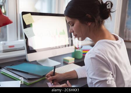Woman taking notes while sitting on her desk Stock Photo