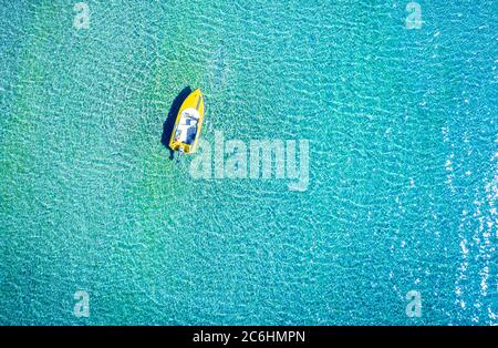 Aerial photo of a yellow lonely tboat tied up in crystal clear turquoise sea water Stock Photo