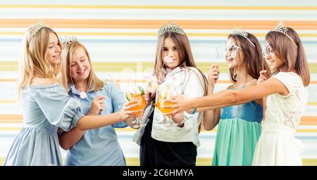 Pretty smiling teenage girls in dresses and crowns knocking beverages together at birthday party Stock Photo