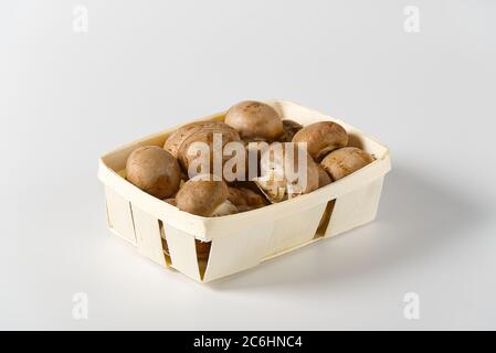 Brown Mushrooms champignons in wooden basket on a light background. Close up. Packed champignons to basket. Stock Photo