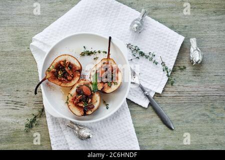Baked pears with nuts, raisins, thyme in a white plate on a wooden table. Stock Photo