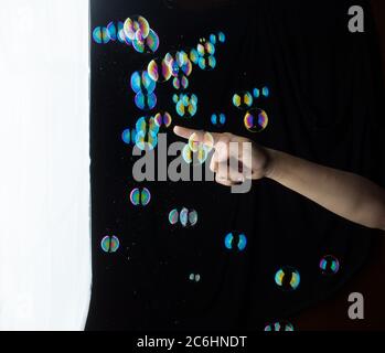 Hand Interacting with Colorful Floating Soap Bubbles. Stock Photo