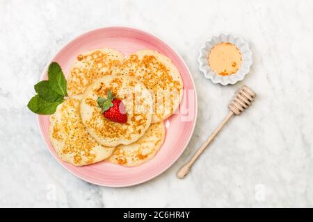 Pancakes with one strawberry on top on a pink plate and on a marble table in a top view Stock Photo