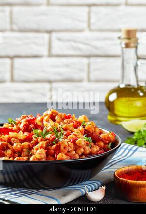 Garbanzos fritos, hot Chickpea stew with chorizo, tomatoes and spices in a black bowl on a concrete table with ingredients at the background of brick Stock Photo