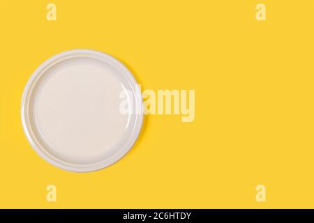 A disposable white plate on a yellow background with copy space Stock Photo