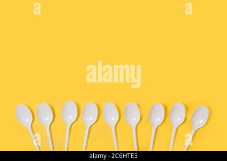 Disposable white plastic spoons on a yellow background in a top view Stock Photo
