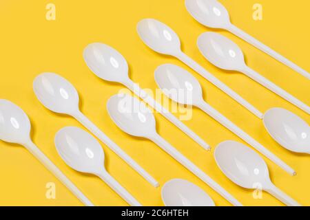 Disposable white plastic spoons on a yellow background in a top view Stock Photo