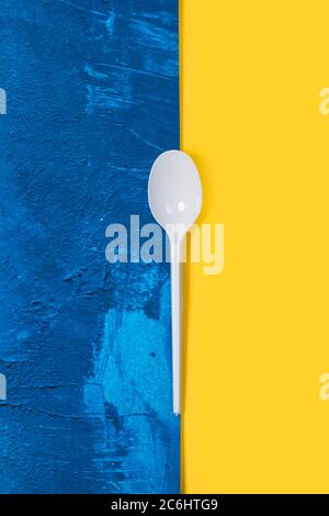 Disposable white plastic spoon on a classic blue and yellow background Stock Photo
