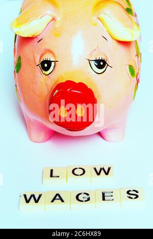 Financial concept image. Difficulty of living on low wages.  Sad looking piggy bank.  Gig economy. No savings.  words 'low wages' on tiles.  Idea shor Stock Photo