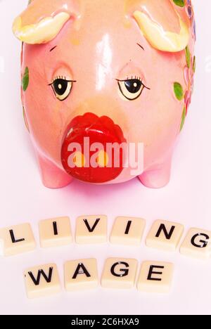 Financial concept image. Difficulty of living on low wages.  Sad looking piggy bank.  Gig economy. No savings.  words 'living wage' on tiles.  Idea sh Stock Photo