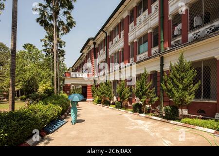 Oblique view of accommodation block for students at Yangon University with student wearing green and holding a green umbrella. Yangon University, Yang Stock Photo