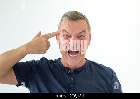 Angry man making a gun gesture pointing to his head as he yells at the camera isolated on white Stock Photo