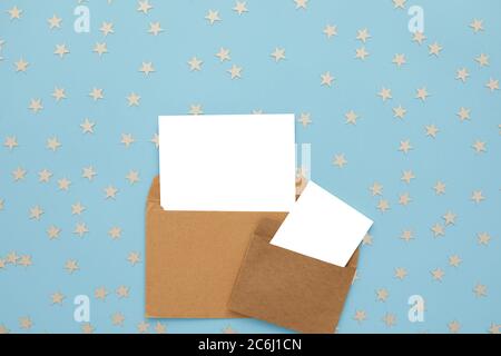 two white blank cards in kraft brown paper envelope on blue background with confetti. Holiday mockup. Top view. Stock Photo