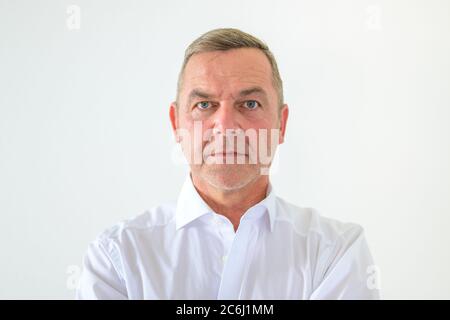 Serious middle-aged man with deadpan expression staring intently at the camera in a head and shoulders portrait on white Stock Photo