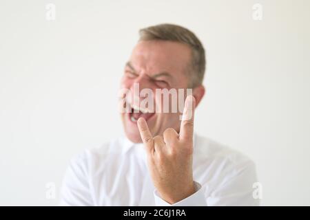 Angry middle-aged man making a Horns gesture with focus to his hand in a head and shoulders portrait on white Stock Photo