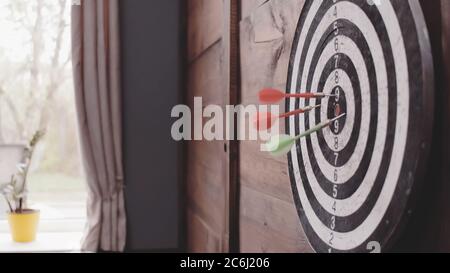 Three Darts arrows hit the bullseye. Dart board hanging on a wooden wall of home or office. Hit goal or target concept. Close up shot. Tinted image Stock Photo