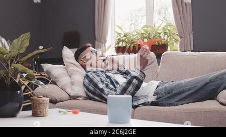 Young man talks mobile phone lying on sofa. Smiling guy communicates via cellular holding darts arrow. Rest concept. Tinted image Stock Photo