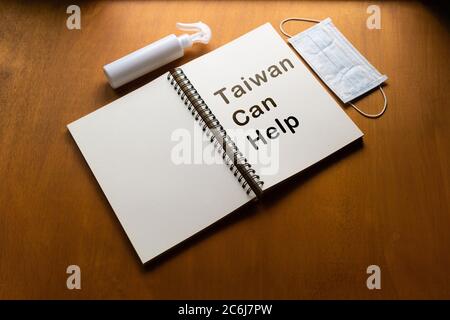 epidemic healthcare concept ,Taiwan Can Help text written on a notebook  ,Alcohol spray and face mask on wooden background Stock Photo