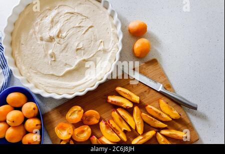 Cooking homemade apricot pie. Slices of fresh apricots for pie on a cutting board, dough in a white baking dish. Stock Photo