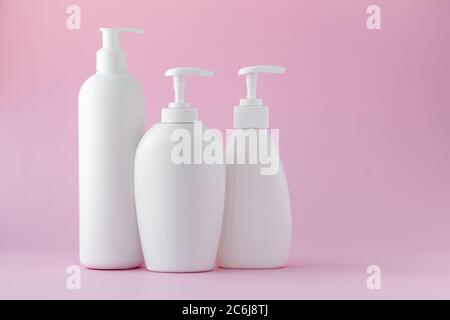 White plastic bottles on a pink background, a set of cosmetic containers with a dispenser. Copy space, empty place for text. Toiletries, pump lotion. Stock Photo