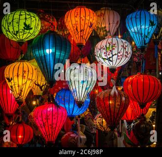 many colors of painted and patterned silk lanterns lit up at night Stock Photo