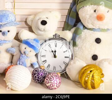 Celebration and New Year decor concept. Toys placed on wooden wall background. Winter holiday decorations, close up. Snowmen, teddy bears and Christmas tree balls near old fashioned alarm clock. Stock Photo