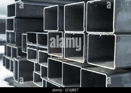 Stacked rolled metal products, wet steel pipes with rectangular cross-section, close-up photo with selective focus Stock Photo