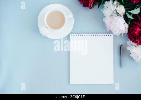 Notebook and a cup of coffee on blue fabric backgroundand peony flowers. Feminine morning concept.n Stock Photo
