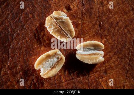 Close up of three grains of traditional thick-rolled oats on old wooden board. Stock Photo