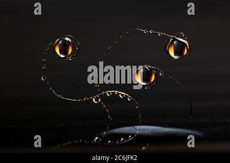 Water drops hang on bent thin metal wires sticking out of the water above the surface against black background. Stock Photo