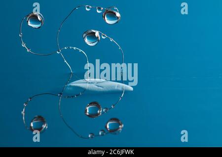 Water drops hang on bent thin metal wires sticking out of the water above the surface against blue background. Stock Photo