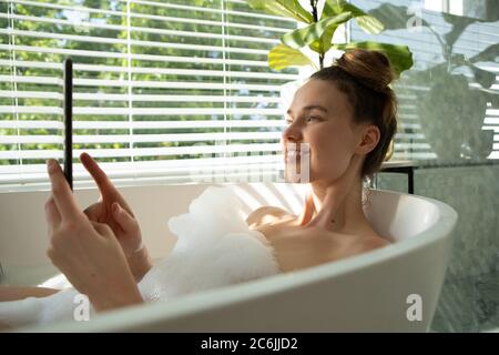 Woman using smartphone in a bathtub Stock Photo