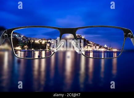 Focused night city view when looking through glasses frame. Black metal glasses looking through colorful cityscape. Glasses for people with visual imp