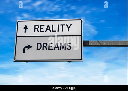 Reality versus dreams. Road sign with words reality and dreams. White two street signs with arrow on metal pole. Directional road. Crossroads Roads Stock Photo