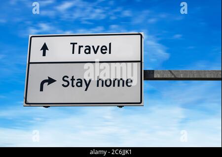 Travel versus stay home. Travel and stay at home concept. White two street signs with arrow on metal pole. Directional road. Crossroads Road Sign, Two Stock Photo