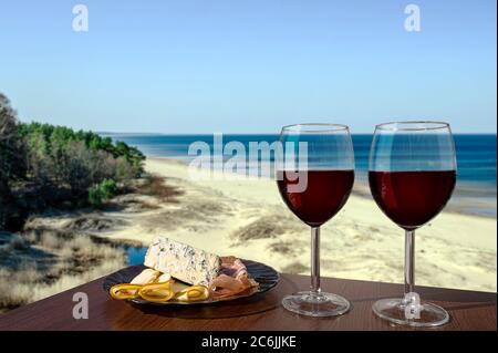 Two glasses of wine with charcuterie assortment with view of beach in Baltic sea. Glass of red wine with different snacks - plate with ham Stock Photo