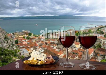 Two glasses of red wine with charcuterie assortment with view of Croatian town Omis with red roofs and blue sea. Glasses of red wine with snacks Stock Photo
