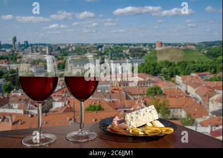 Two glasses of wine with charcuterie assortment on view of Vilnius, Lithuania. Glass of red wine with different snacks - plate with ham, sliced, blue Stock Photo