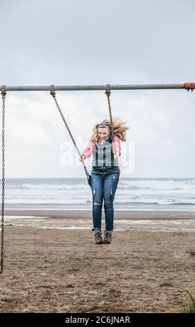 A middle aged woman swinging on a swing set on Seaside Beach, Oregon, USA.